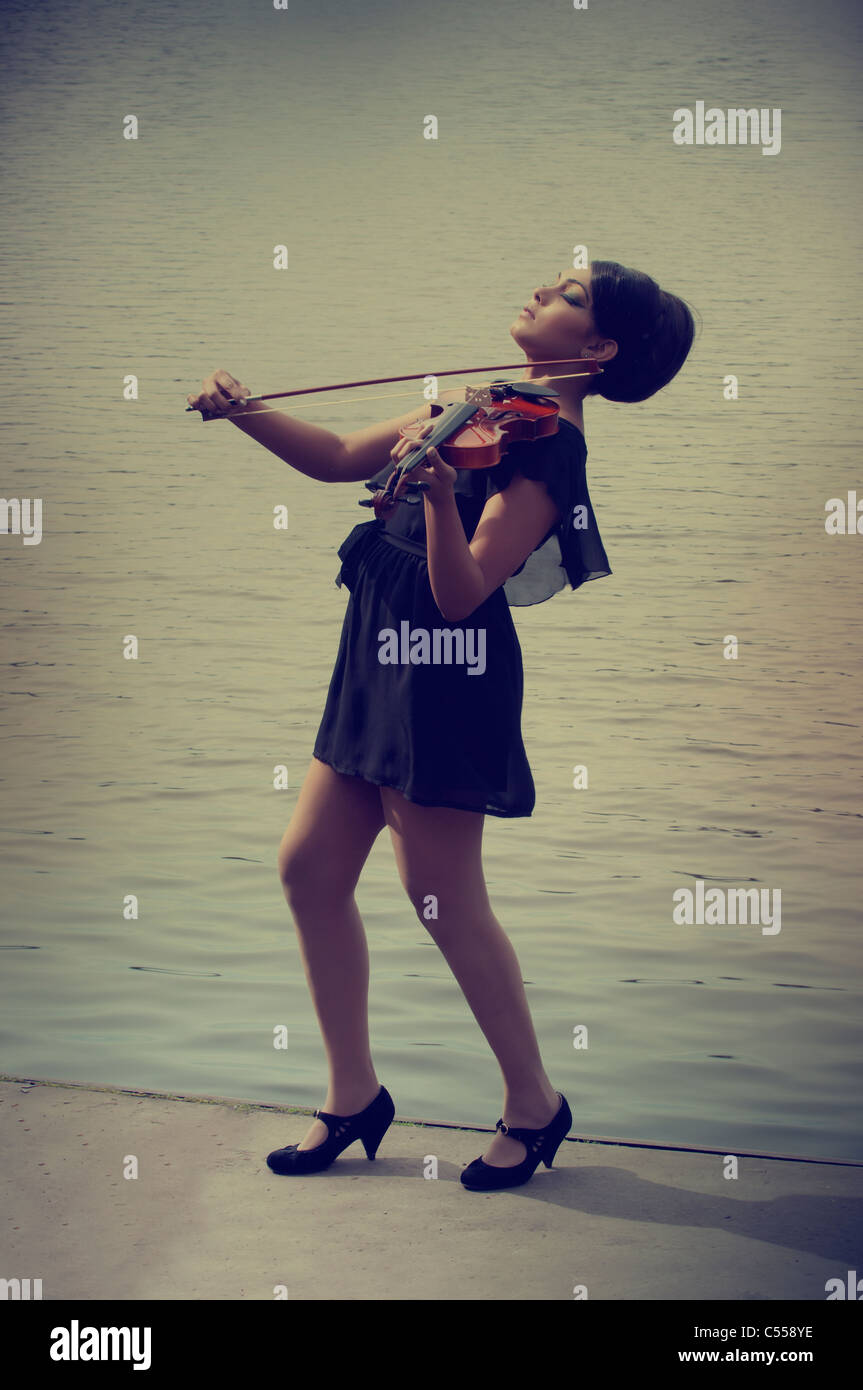 Femme debout au bord du lac à jouer du violon Banque D'Images