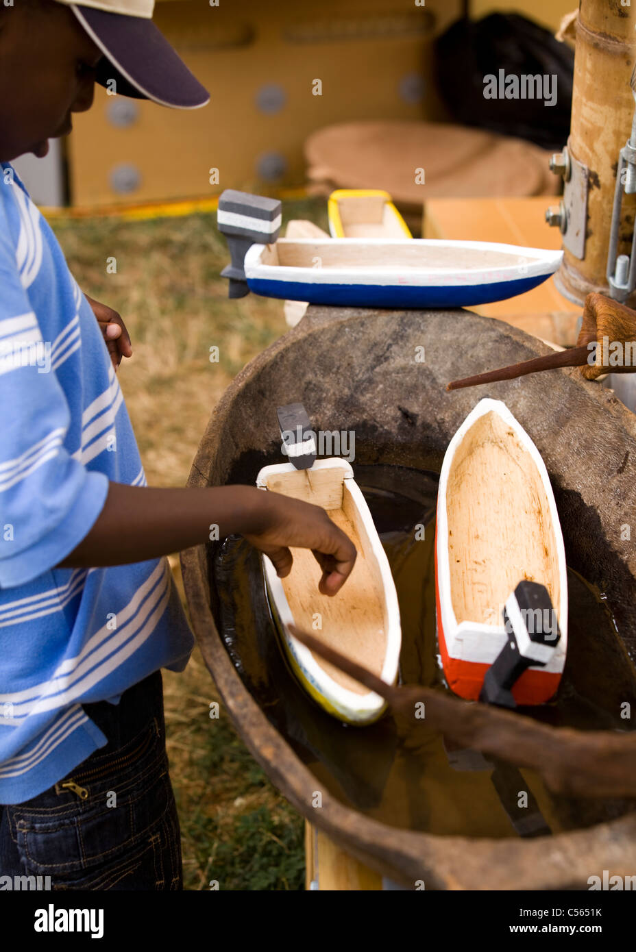 Jeune garçon africain inspecte les bateaux en bois de jouets dans la baignoire d'eau Banque D'Images
