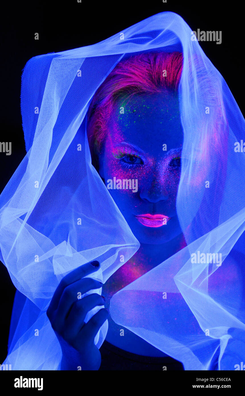 Visage de femme dans l'obscurité avec maquillage peinture fluorescente portant un voile blanc bleu profond sous les lumières noires Banque D'Images