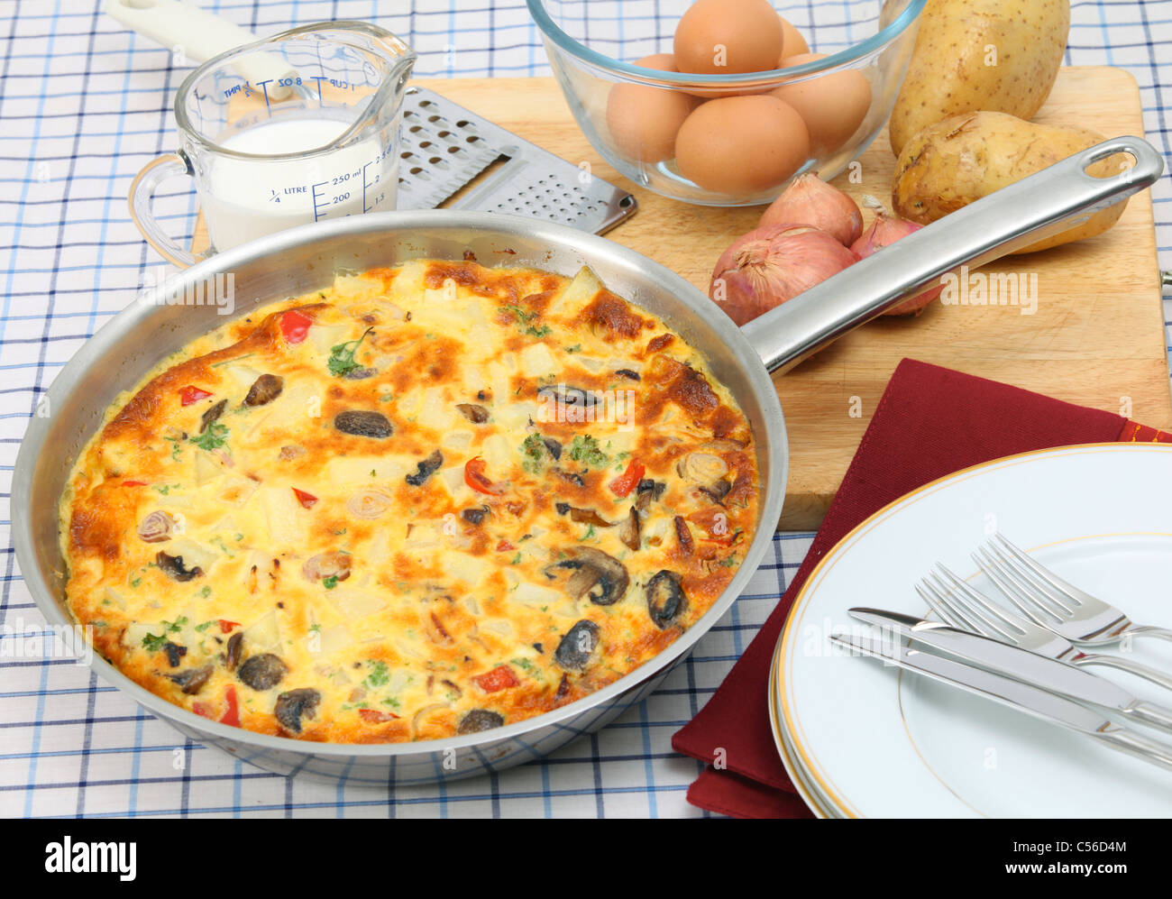 Un petit-déjeuner fraîchement préparé l'omelette espagnole ou de tortilla de patates toujours dans la casserole, avec des ingrédients essentiels derrière Banque D'Images