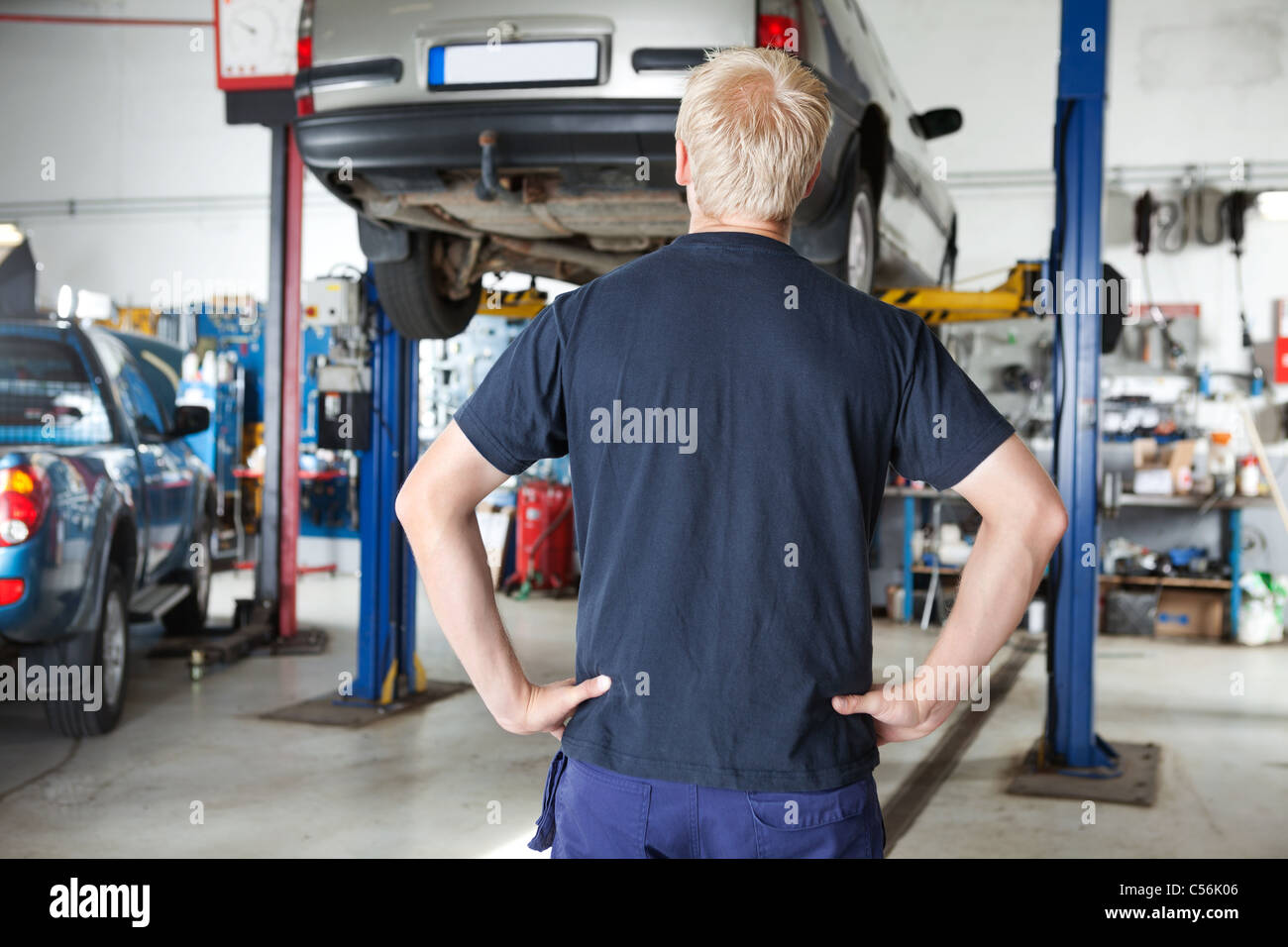 Vue arrière du réparateur de voiture à la voiture à en atelier de réparation automobile avec les mains de taille Banque D'Images