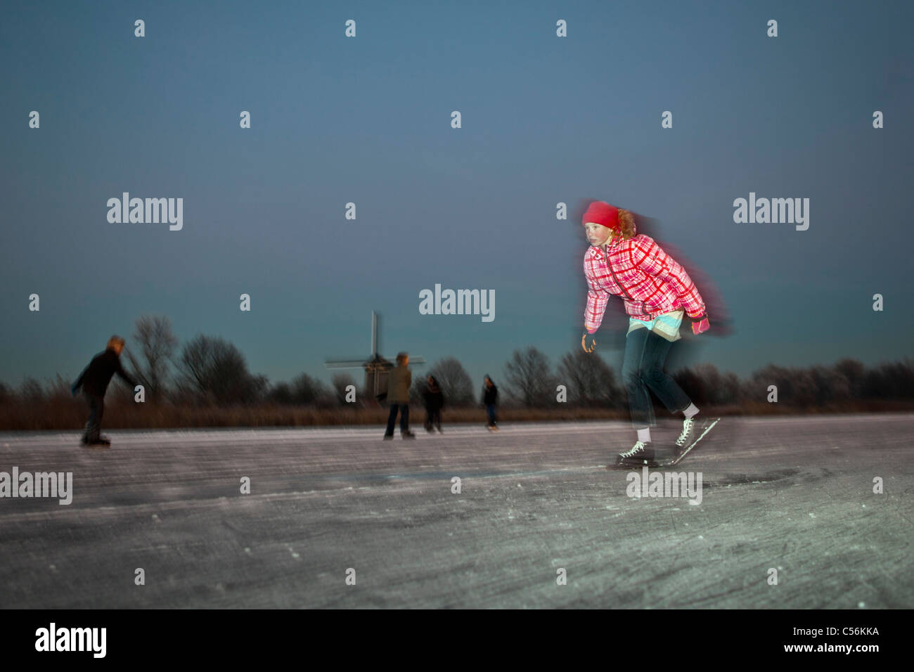 Les Pays-Bas, l'Ankeveen. Fille du patinage sur glace. Moulin à vent d'arrière-plan. Le crépuscule. Flou de mouvement. Banque D'Images