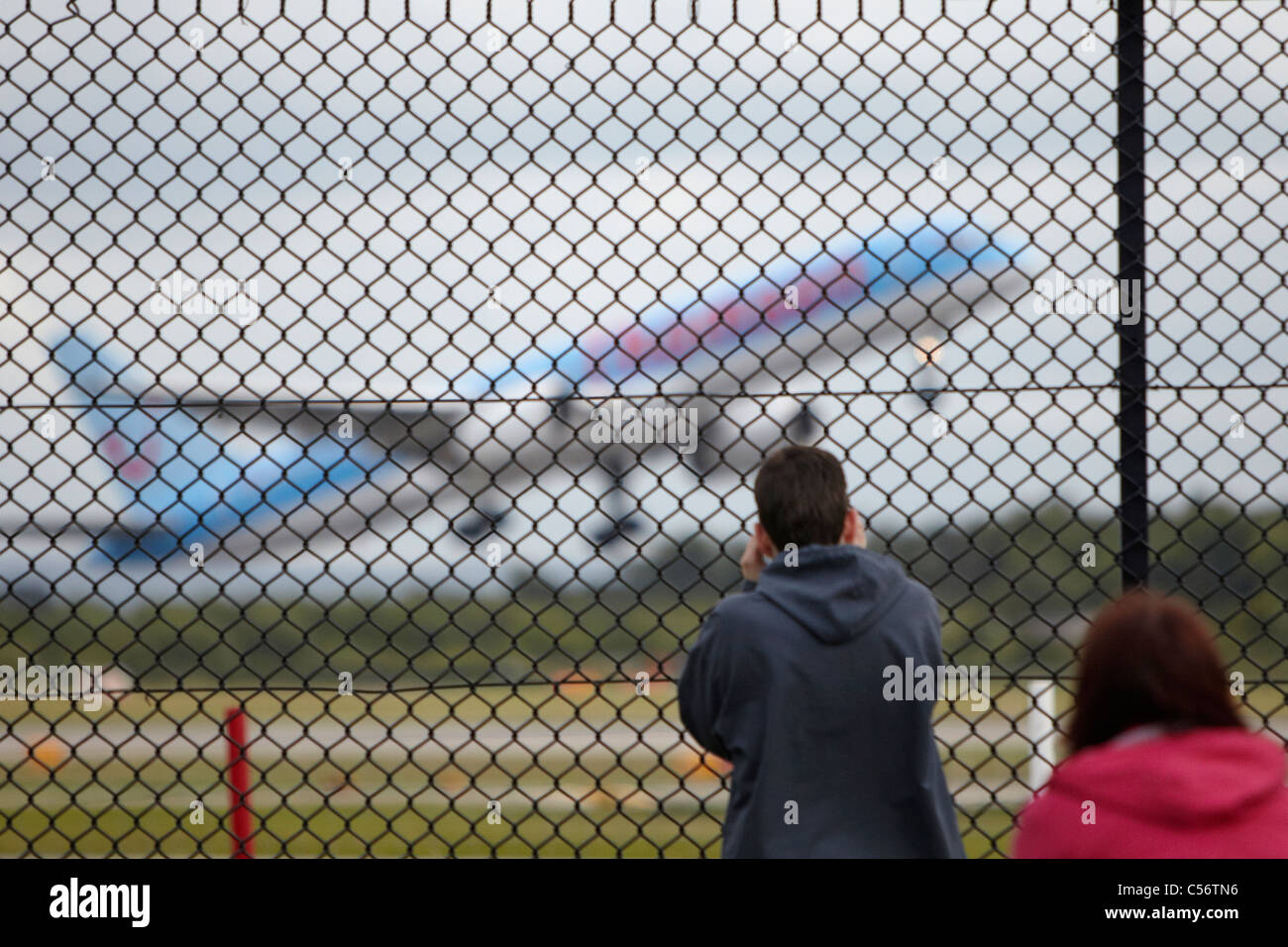 Les gens qui regardent un avion décollant à travers une clôture Banque D'Images