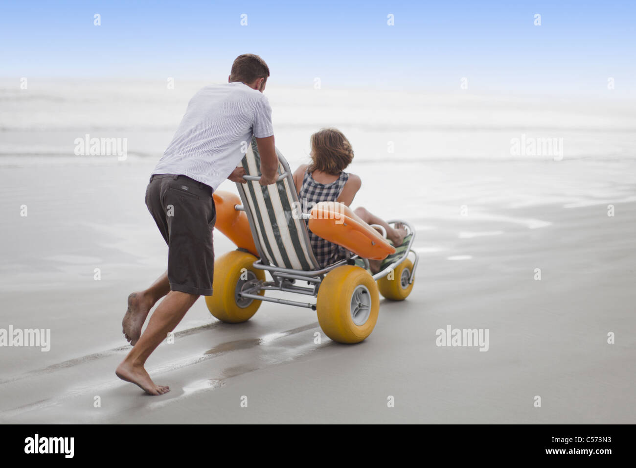 Man pushing petite amie dans le panier on beach Banque D'Images