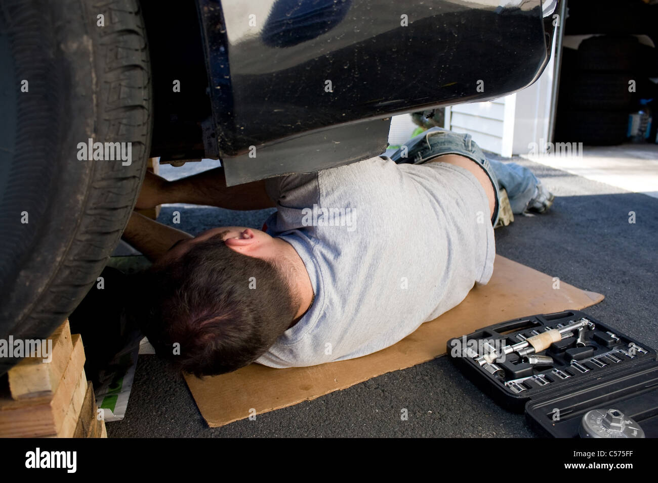 Un jeune homme portant sous une voiture ou faire des réparations sur le véhicule d'entretien. Banque D'Images