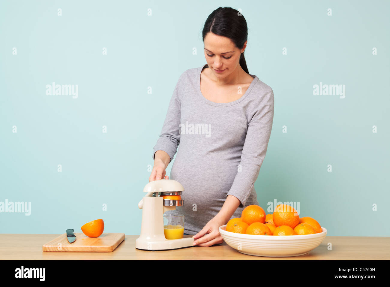 Photo d'une femme enceinte de la semaine 32 dans sa cuisine préparer le jus d'orange fraîchement pressé. Banque D'Images