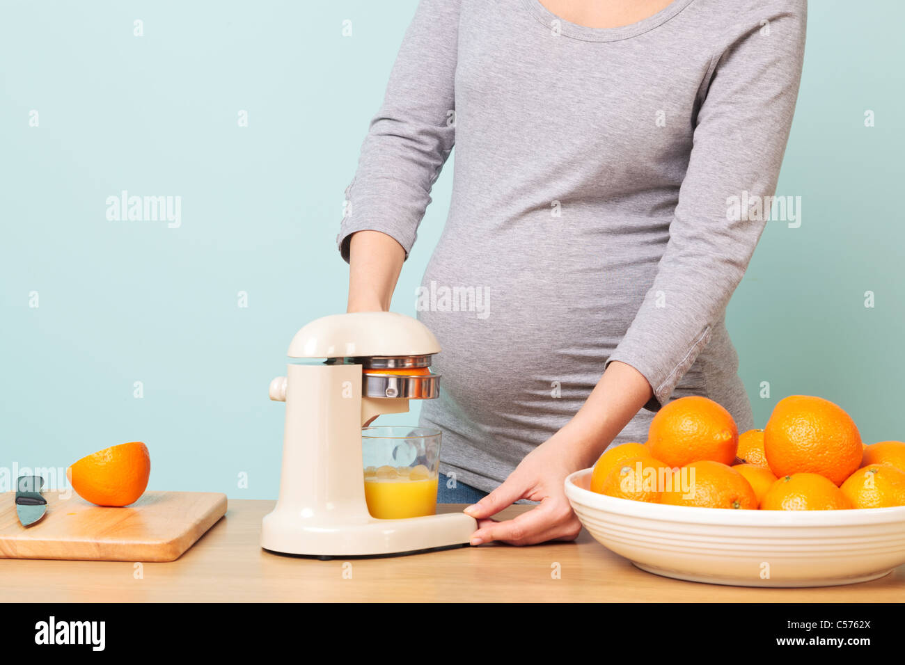 Photo d'une femme enceinte de la semaine 32 dans sa cuisine préparer le jus d'orange fraîchement pressé. Banque D'Images