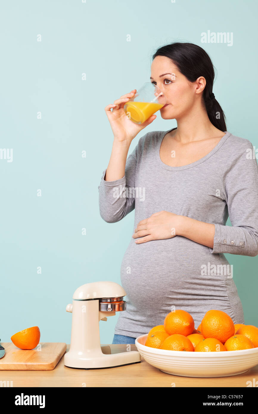 Photo d'une femme enceinte de la semaine 32 dans sa cuisine de boire du jus d'orange fraîchement pressé. Banque D'Images