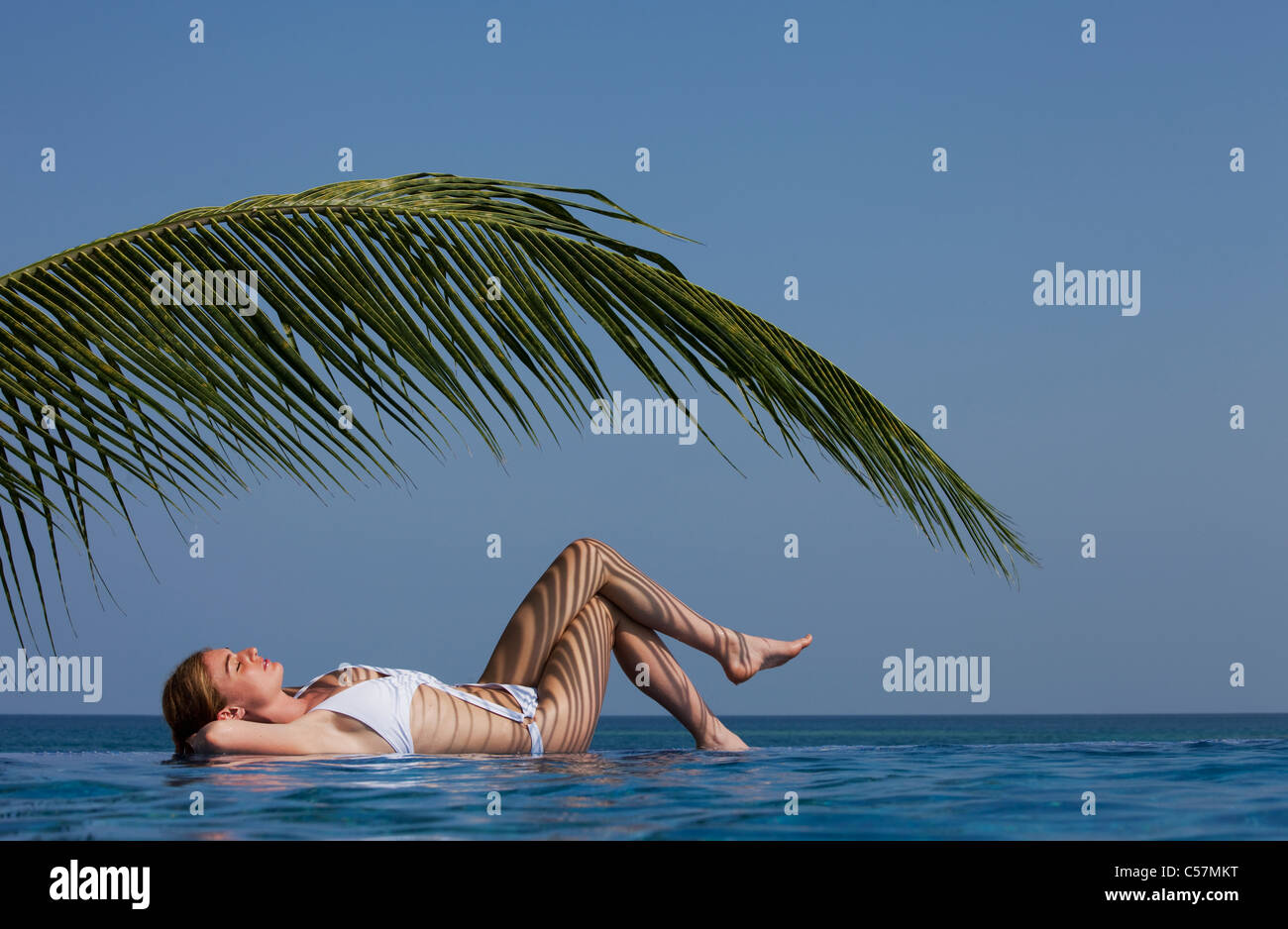 Femme de palmier par piscine à débordement Banque D'Images