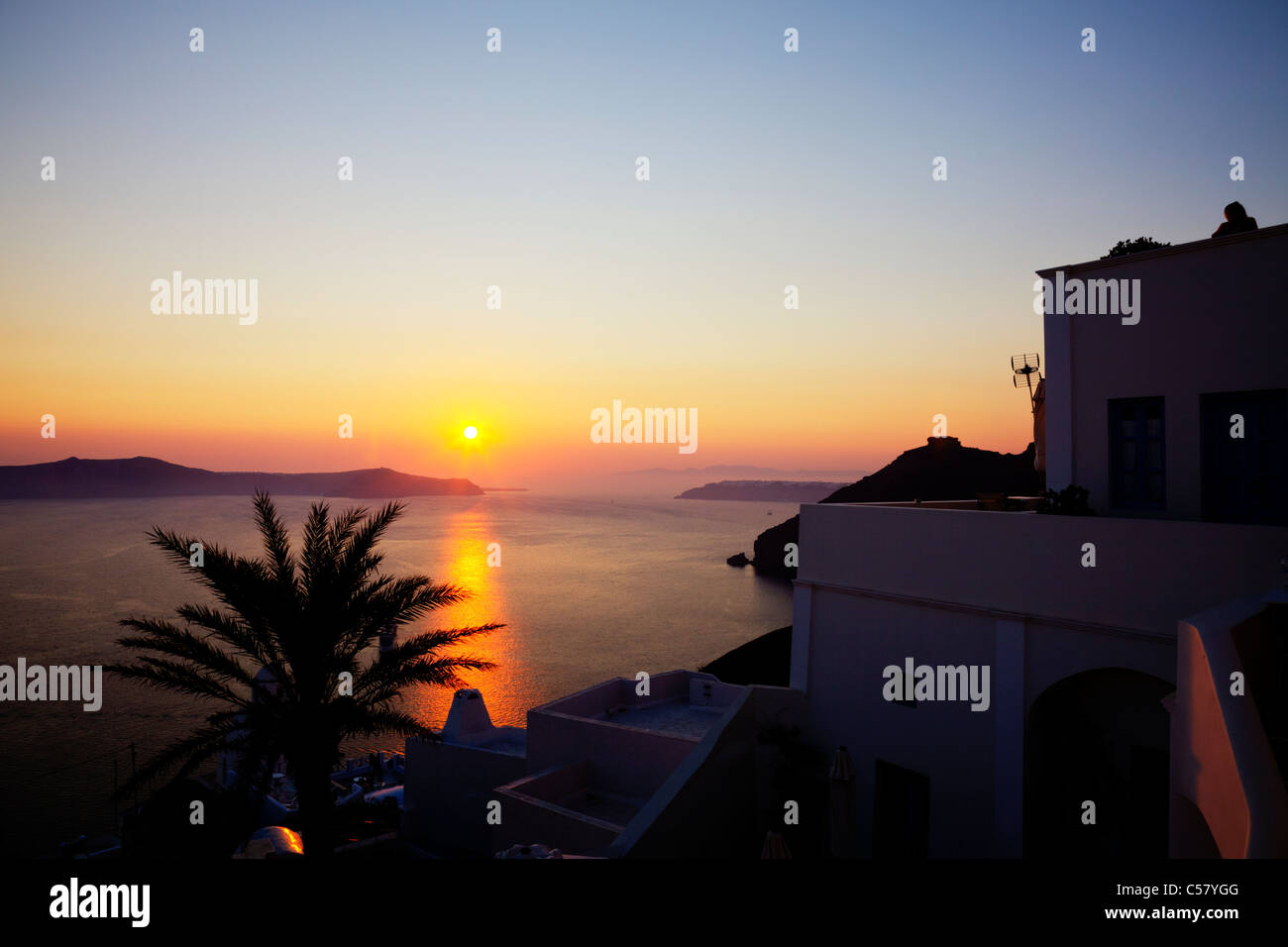 Thira, Santorin, île grecque, la Grèce, l'emblématique coucher de soleil sur caldera cyclades palmier brise le reflet Banque D'Images