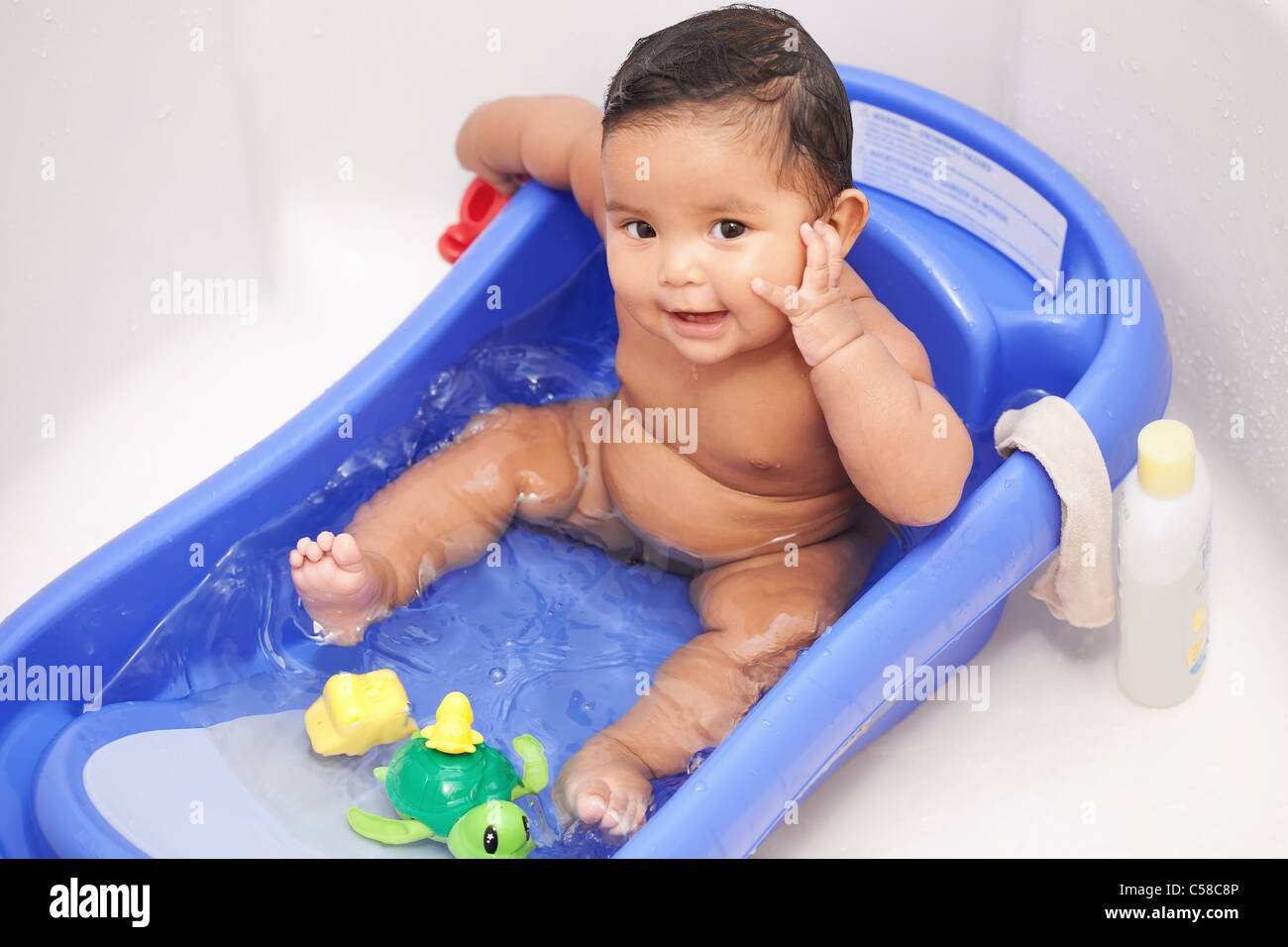 Happy baby girl sitting en toute sécurité dans une baignoire pour bébé avec jeux d'eau et laver le linge prêt à être nettoyé Banque D'Images