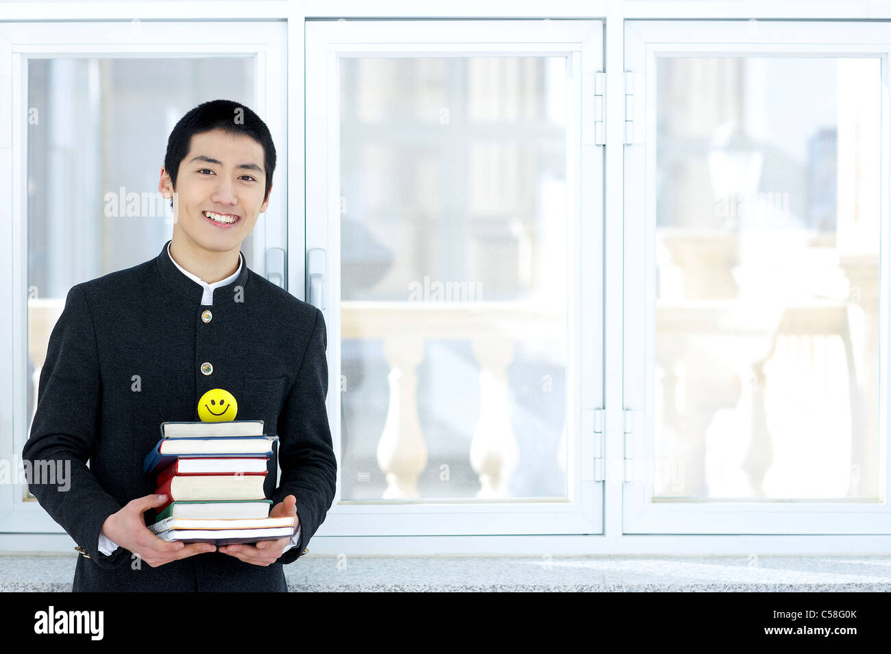 Portrait of teenage boy standing in college, holding books Banque D'Images
