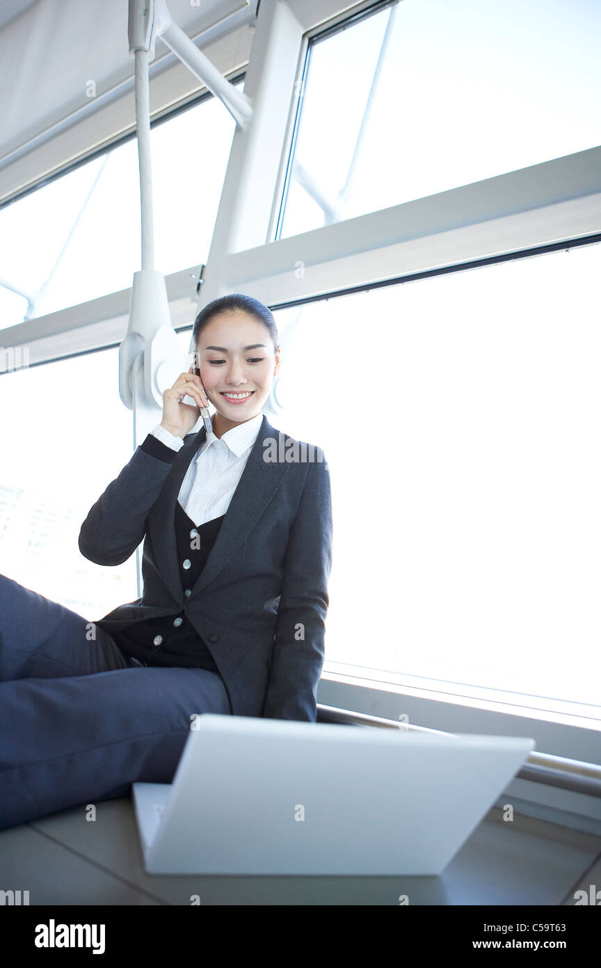 Vue de côté businesswoman talking on mobile phone, using laptop Banque D'Images