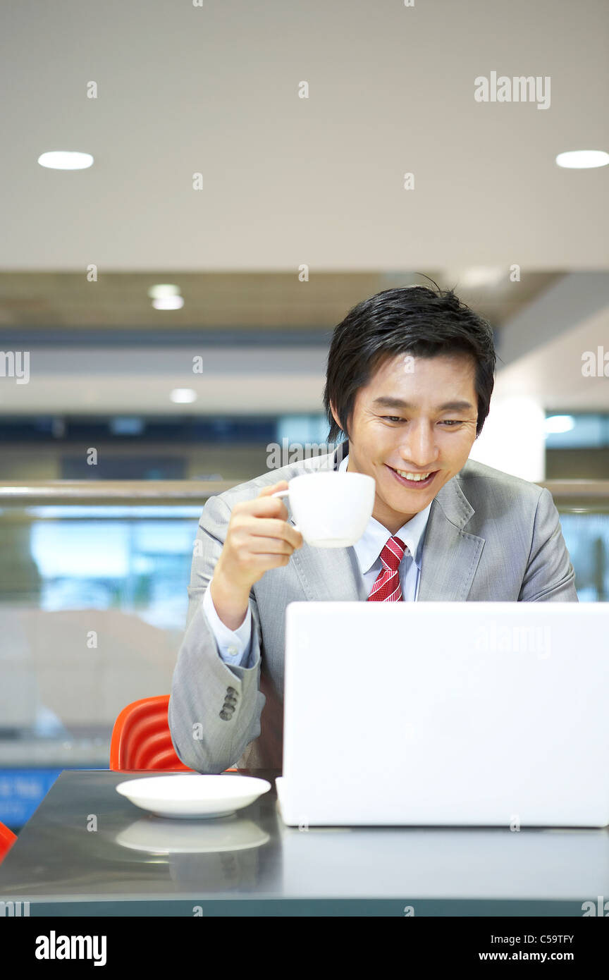 Businessman with tasse et soucoupe en utilisant un ordinateur portable, Banque D'Images