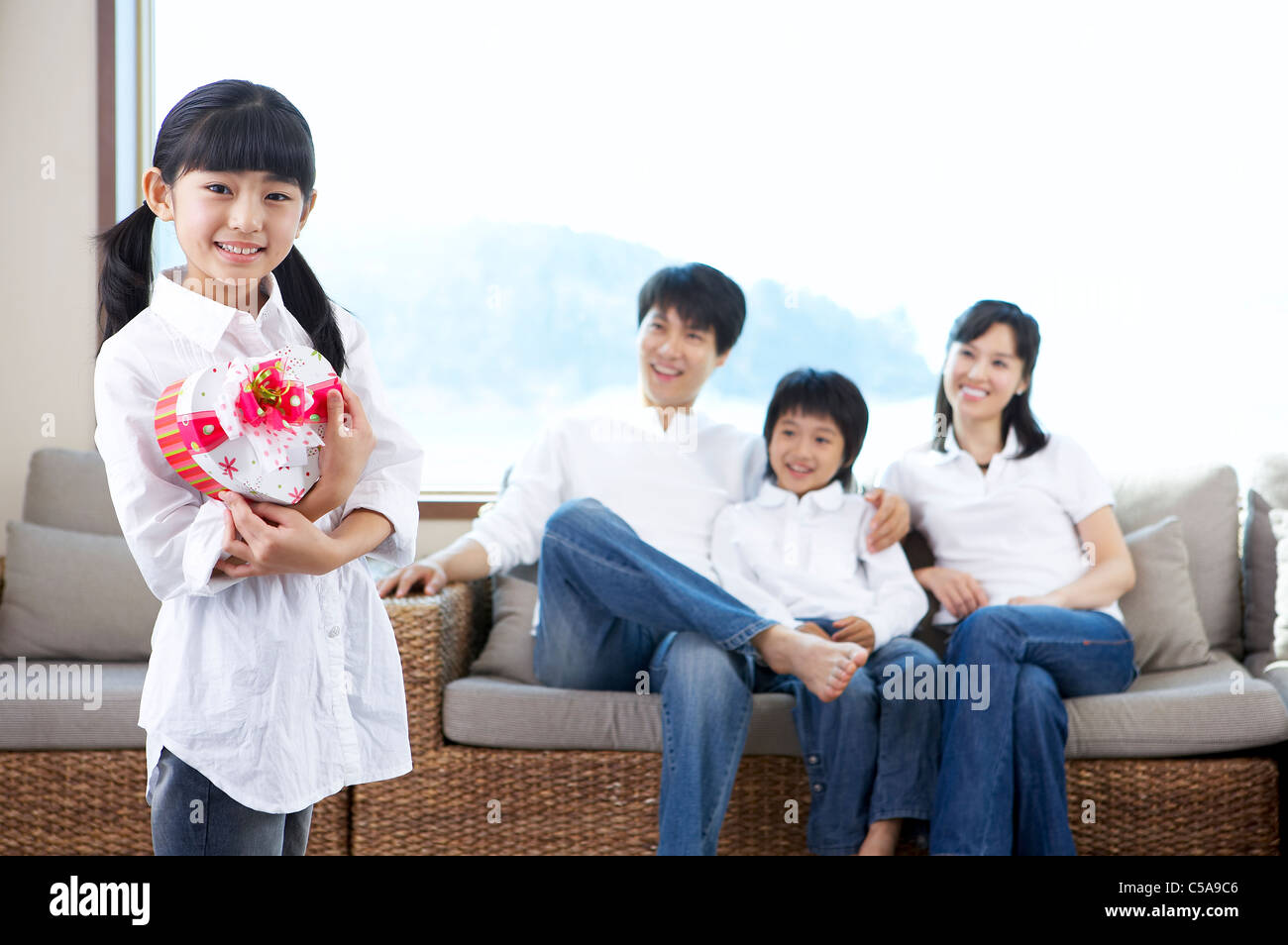 Portrait de fille holding heart shape box, tandis que les parents et le frère de sitting on sofa Banque D'Images