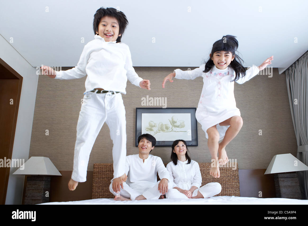 Portrait des enfants sautant sur le lit, tandis que les parents à la recherche Banque D'Images