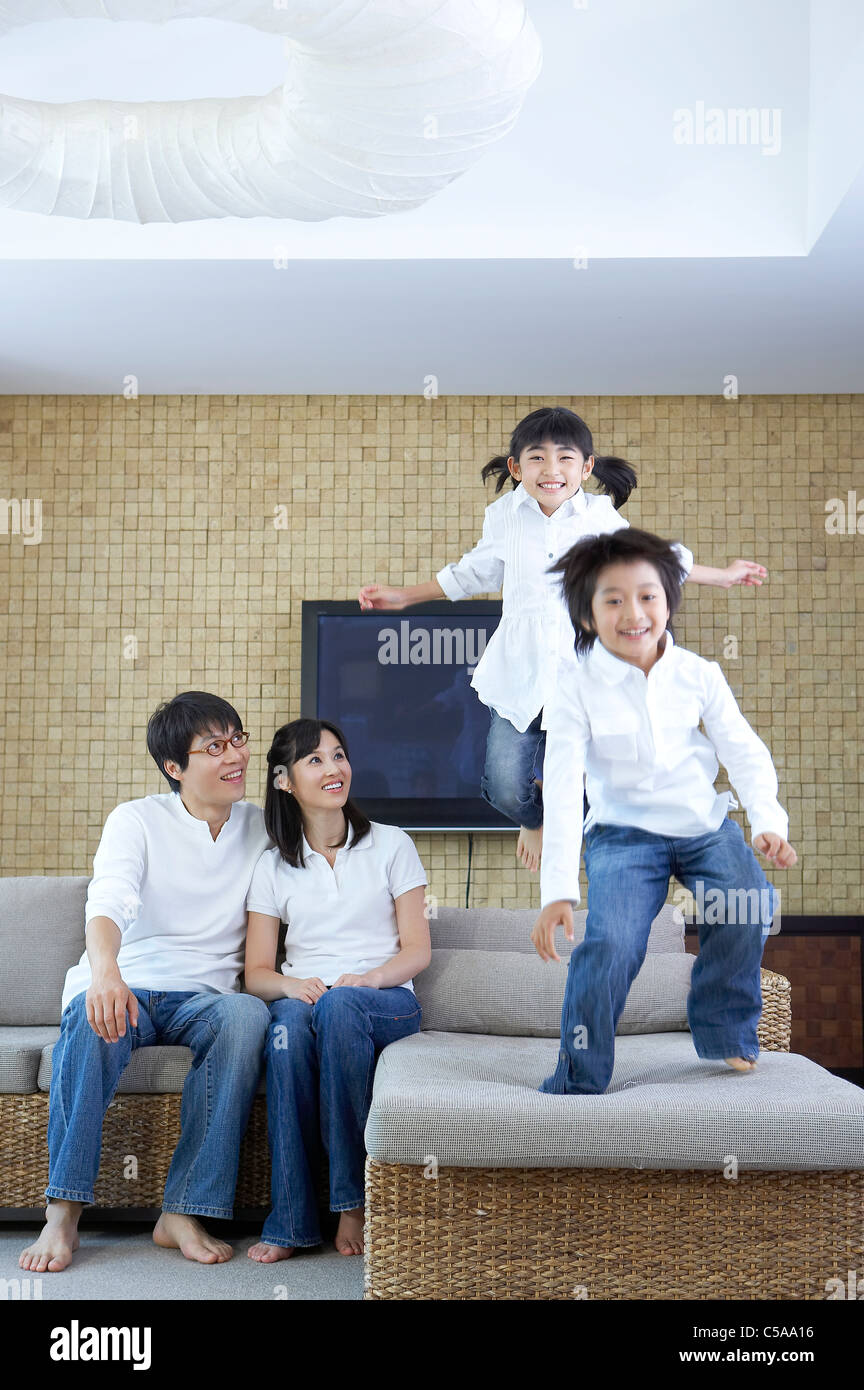 Portrait des enfants sautant sur canapé, tandis que les parents à la recherche Banque D'Images