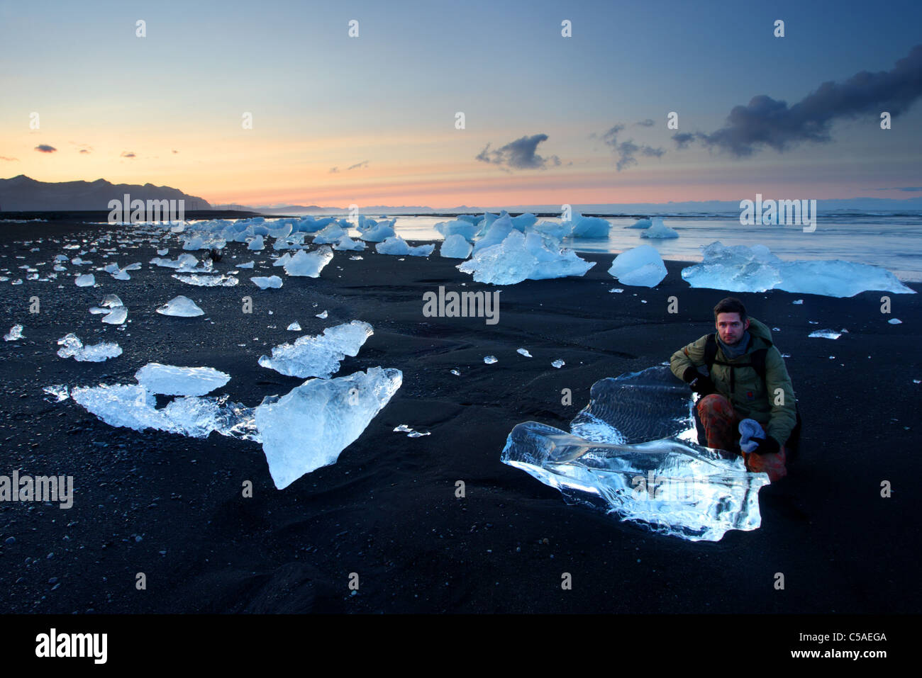 Un homme comme comparaison avec des morceaux de glace de glacier sur la plage de sable noir, l'Islande, Jökulsárlón. Banque D'Images