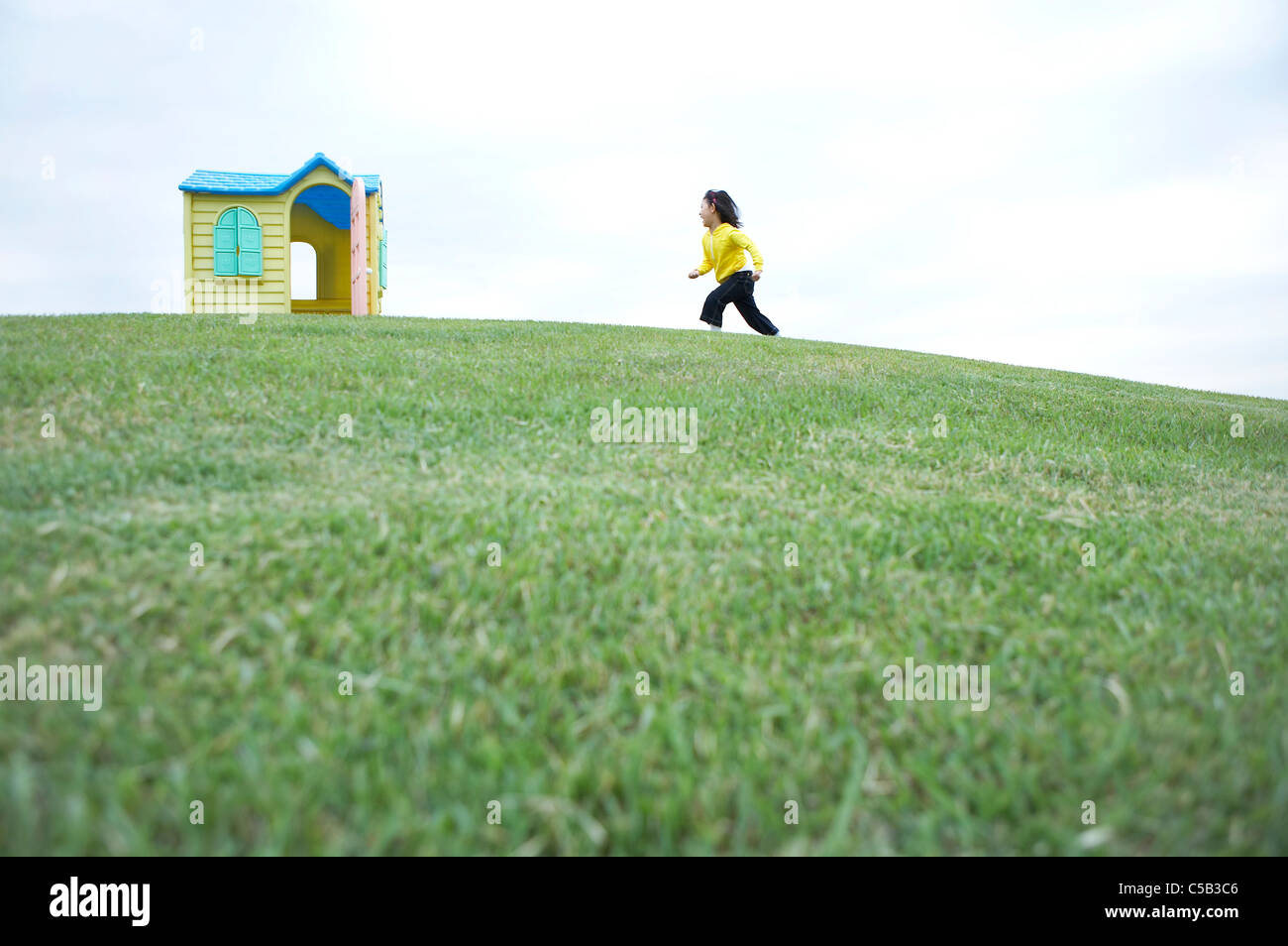 Vue de côté de fille courir sur la pelouse vers toy house Banque D'Images