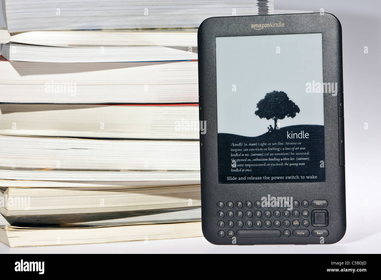 Amazon Kindle e-reader à côté d'une pile de livres traditionnels en désordre Banque D'Images