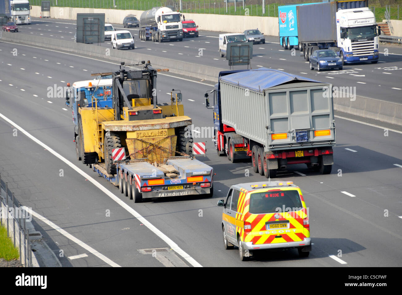 Chargeur faible poids lourds camion remorque articulée & camion chargé de matériel de construction à l'échelle de charge en surplomb en voiture sur l'autoroute britannique avec escort van Banque D'Images