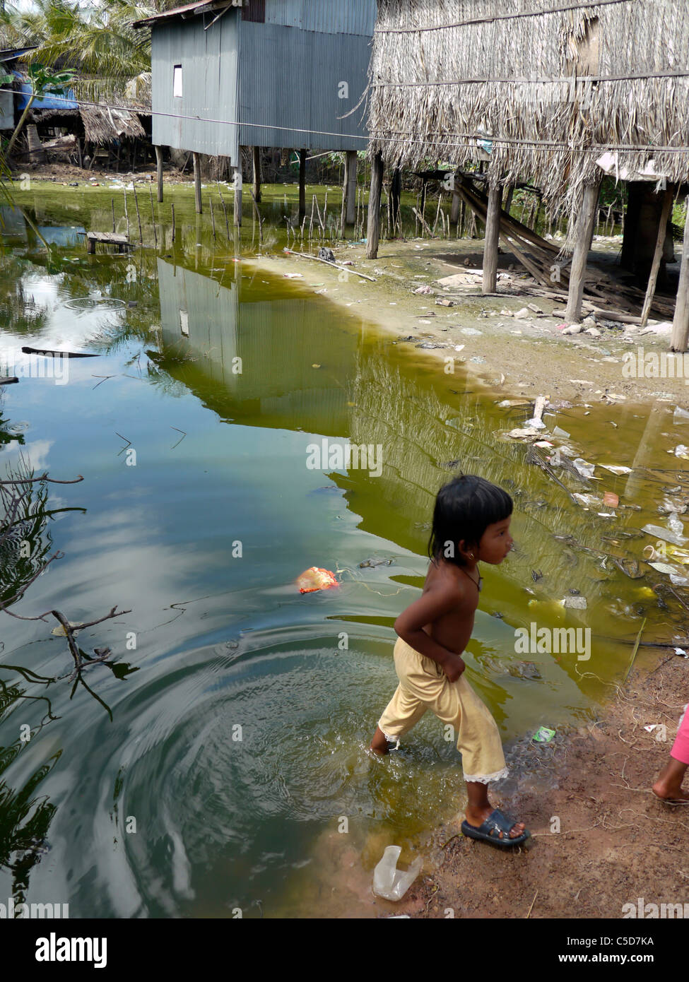 Cambodge fille jouant dans la pollution de l'étang. Don Tok village, Kampot, se trouve à côté de l'estuaire d'une rivière et est souvent inondés par l'eau de mer. Banque D'Images