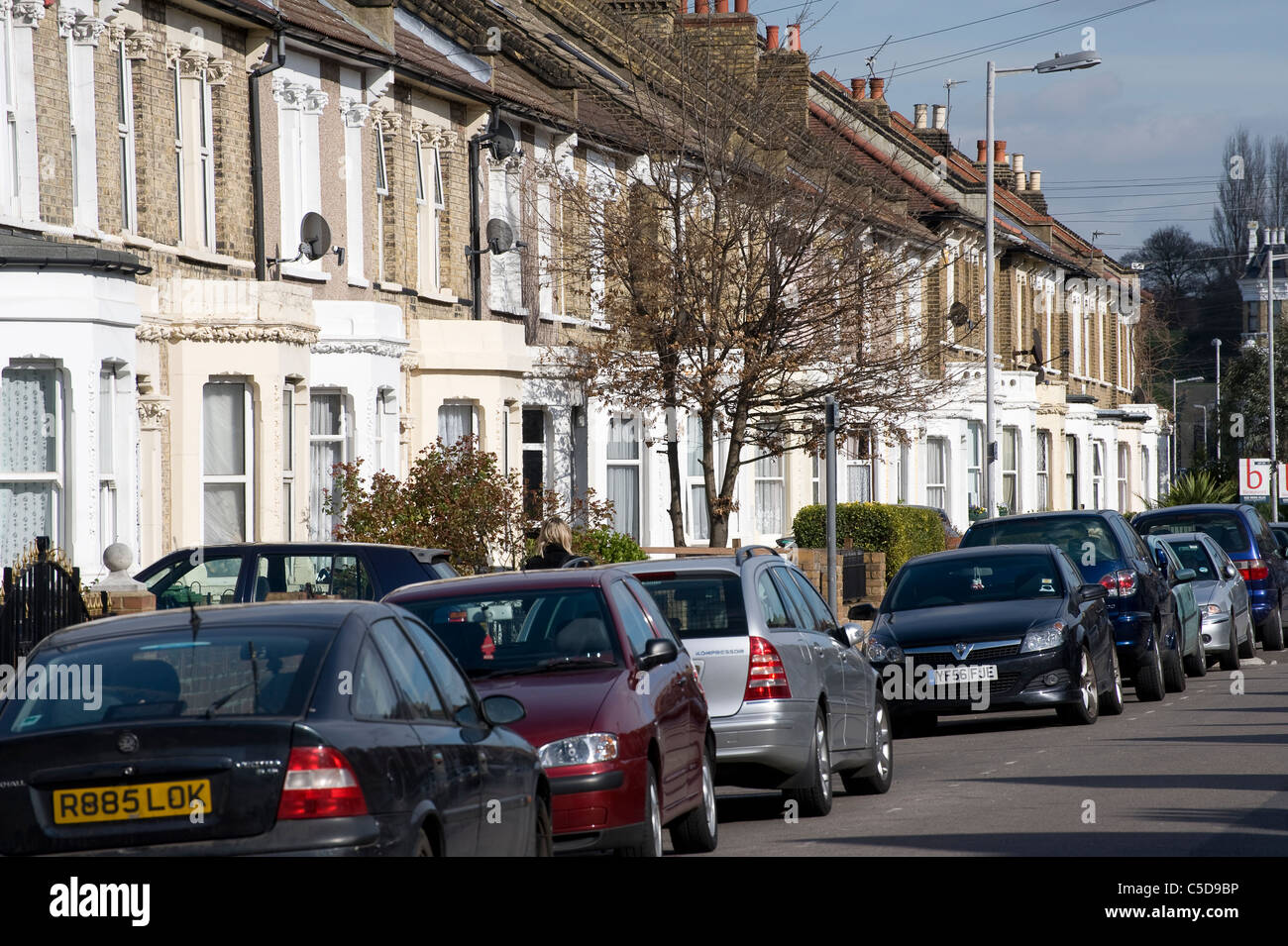 Voitures garées devant des maisons en terrasse sur une rue de banlieue en Angleterre. Banque D'Images