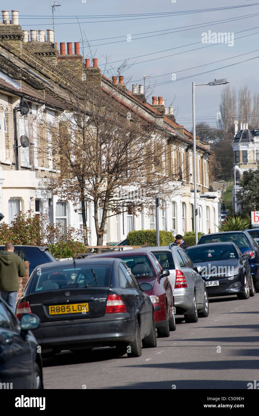 Voitures garées devant des maisons en terrasse sur une rue de banlieue en Angleterre. Banque D'Images