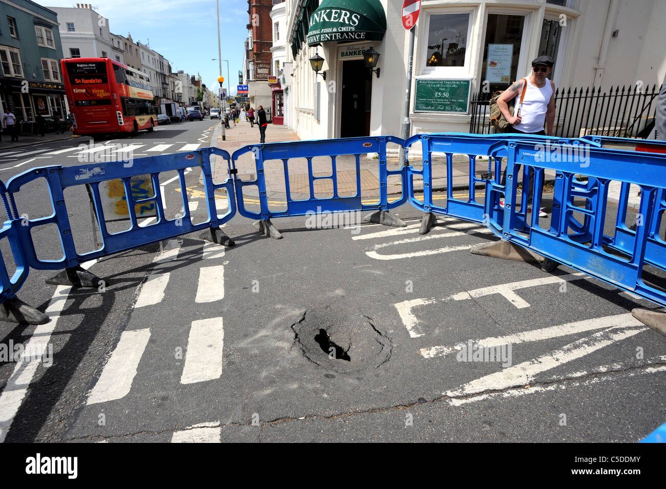 Une barrière de sécurité est mis autour d'un trou qui apparaît soudainement dans une rue animée à Hove Banque D'Images