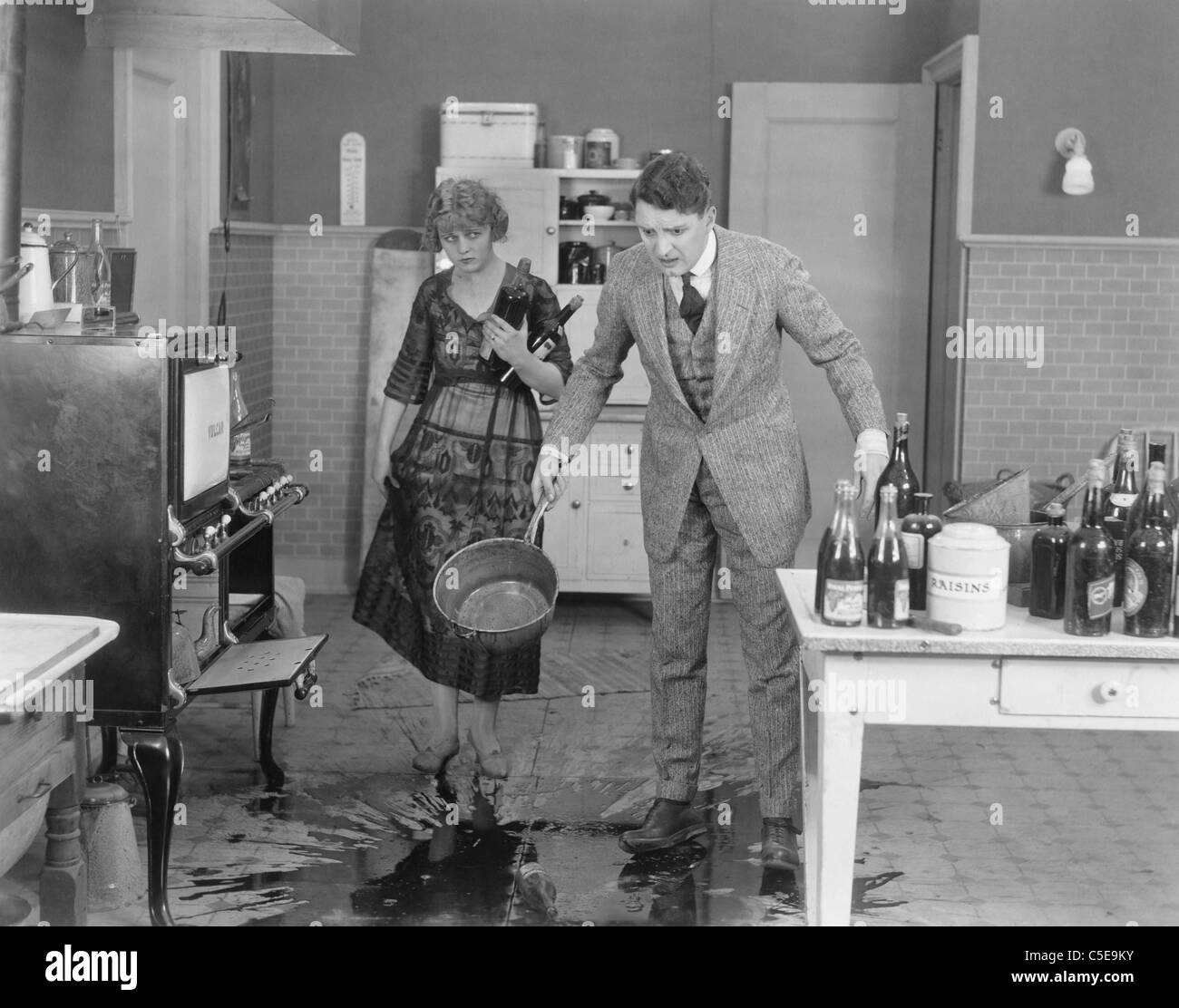 L'homme et la femme regardant le liquide répandu sur le sol de la cuisine Banque D'Images