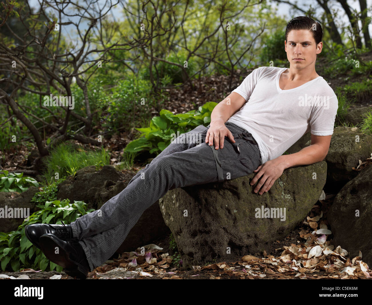Photo d'un élégant jeune homme assis sur un rocher dans un jardin Banque D'Images