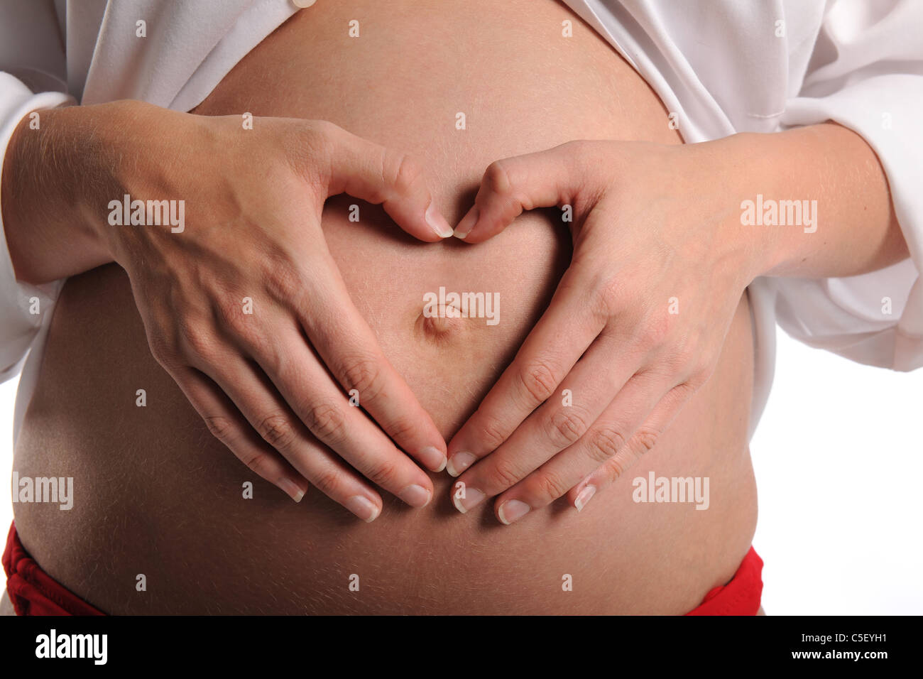 Pregnant woman making heart shape avec les mains sur son estomac isolé sur fond blanc Banque D'Images