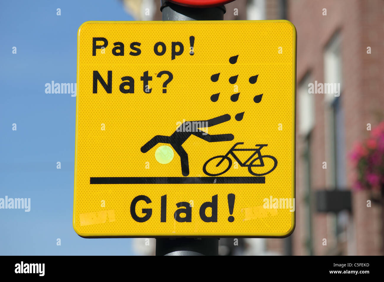 Een verkeersbord met de tekst PAS OP NAT ? Heureux ! En een tekening van een fiets en een persoon vallend Banque D'Images