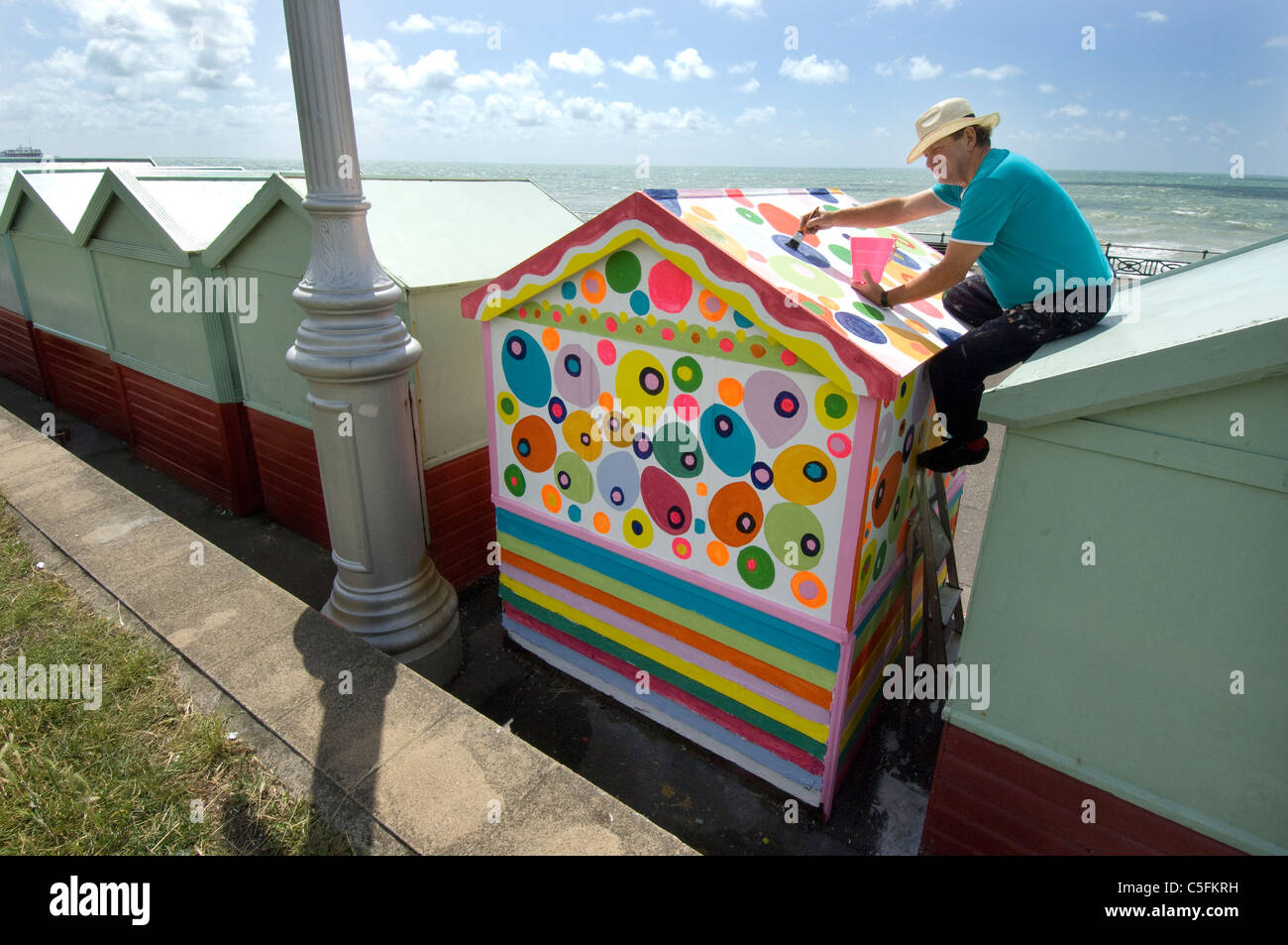 Un homme d'âge moyen de défier les règles et qu'il sa peinture Brighton Beach Hut dans la non-régulation des taches colorées. Banque D'Images