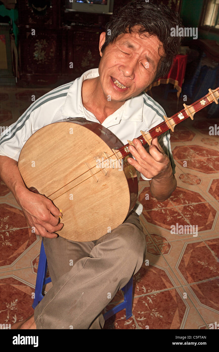 Viet Trinh Quang, 53 ans, joue un instrument à cordes, connu comme une lune luth en son domicile de Tho Ha village, Vietnam Banque D'Images