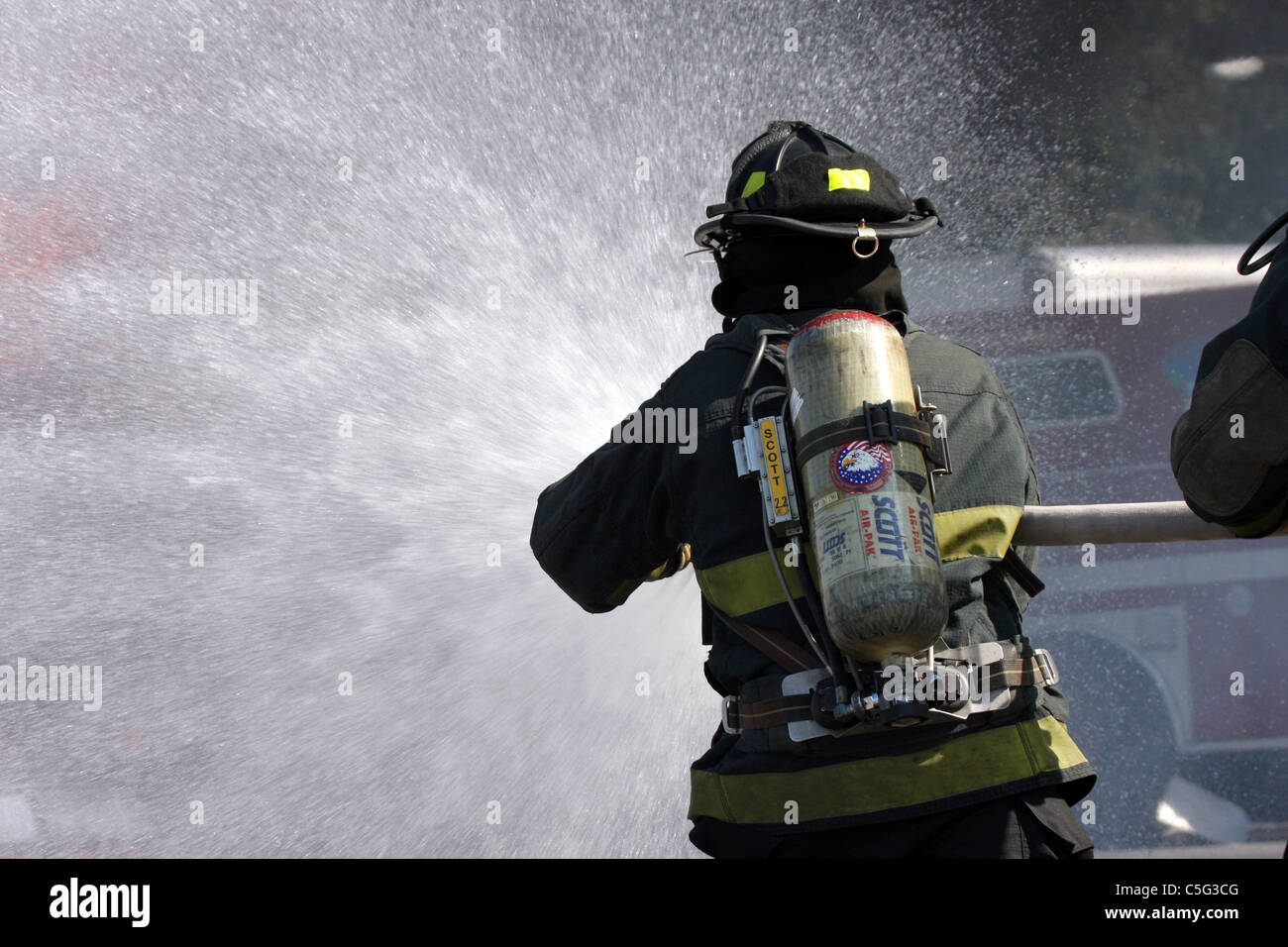Deux pompiers pour éteindre un incendie avec le camion de pompiers en arrière-plan Banque D'Images