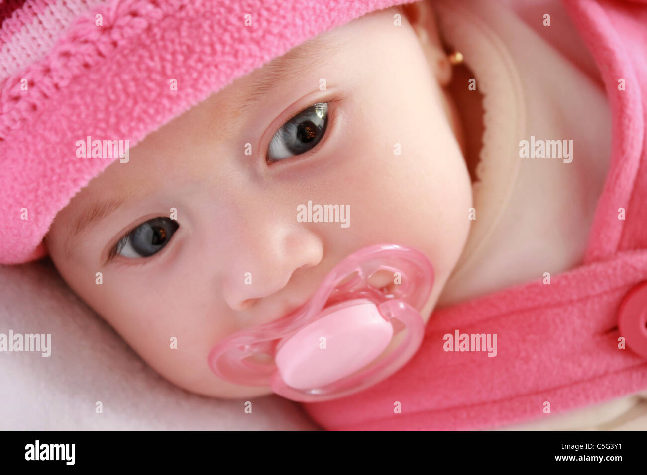Une Jolie Petite Fille Aux Yeux Bleus Et Roses Les Vetements Qui Trainent Sur Un Lit De Bebe Avec Une Tetine Dans Sa Bouche Photo Stock Alamy