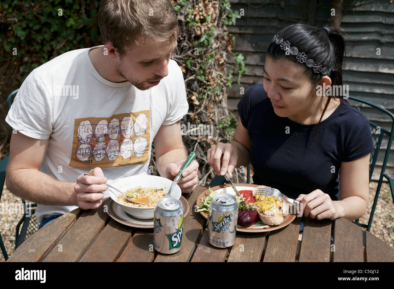 Garçon anglais de manger la nourriture thaïe et Thai girl eating French food England UK Banque D'Images
