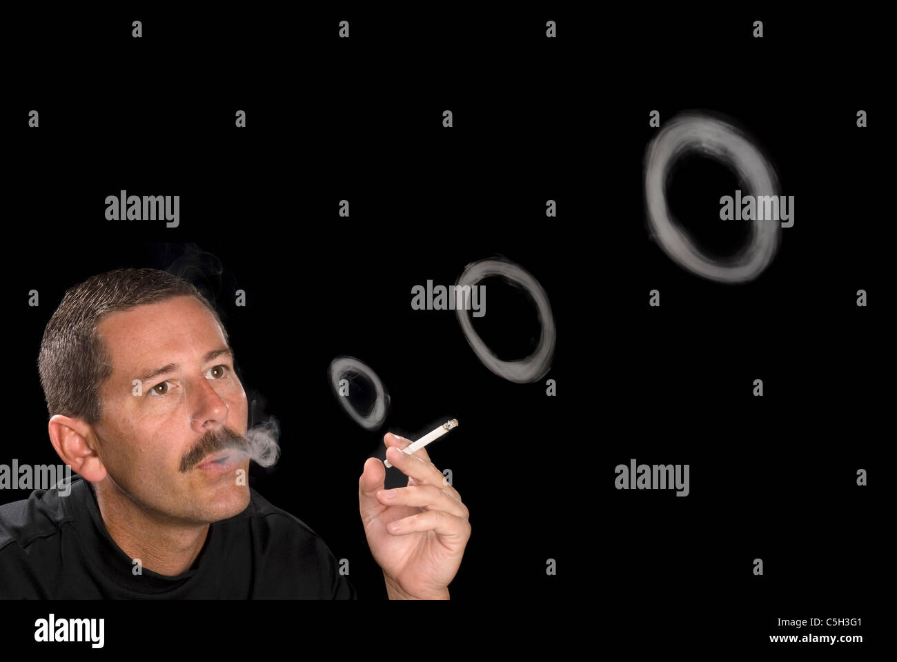 Un homme fume une cigarette coups des ronds de fumée contre une toile de fond noir. Banque D'Images