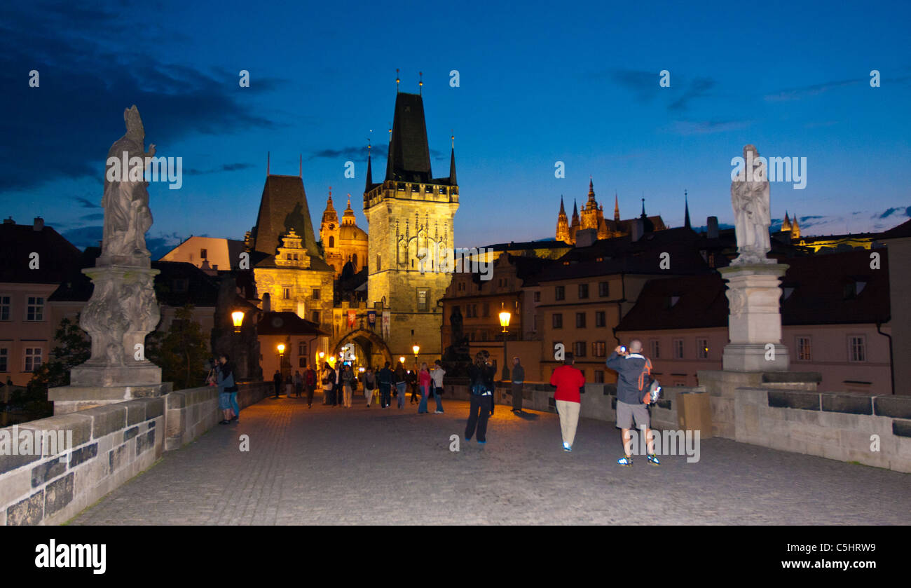 Quelques touristes sur le pont Charles au crépuscule dans Prague. Les beaux bâtiments antiques sont éclairés en lumière dorée. Banque D'Images