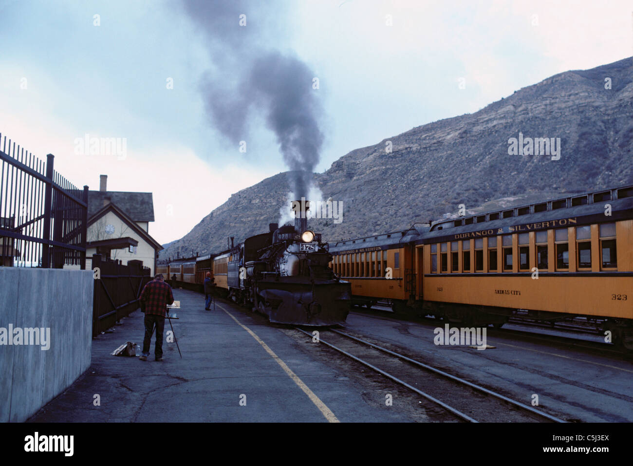 Un homme peint à côté d'un vieux train à vapeur en face de falaises rocheuses Banque D'Images