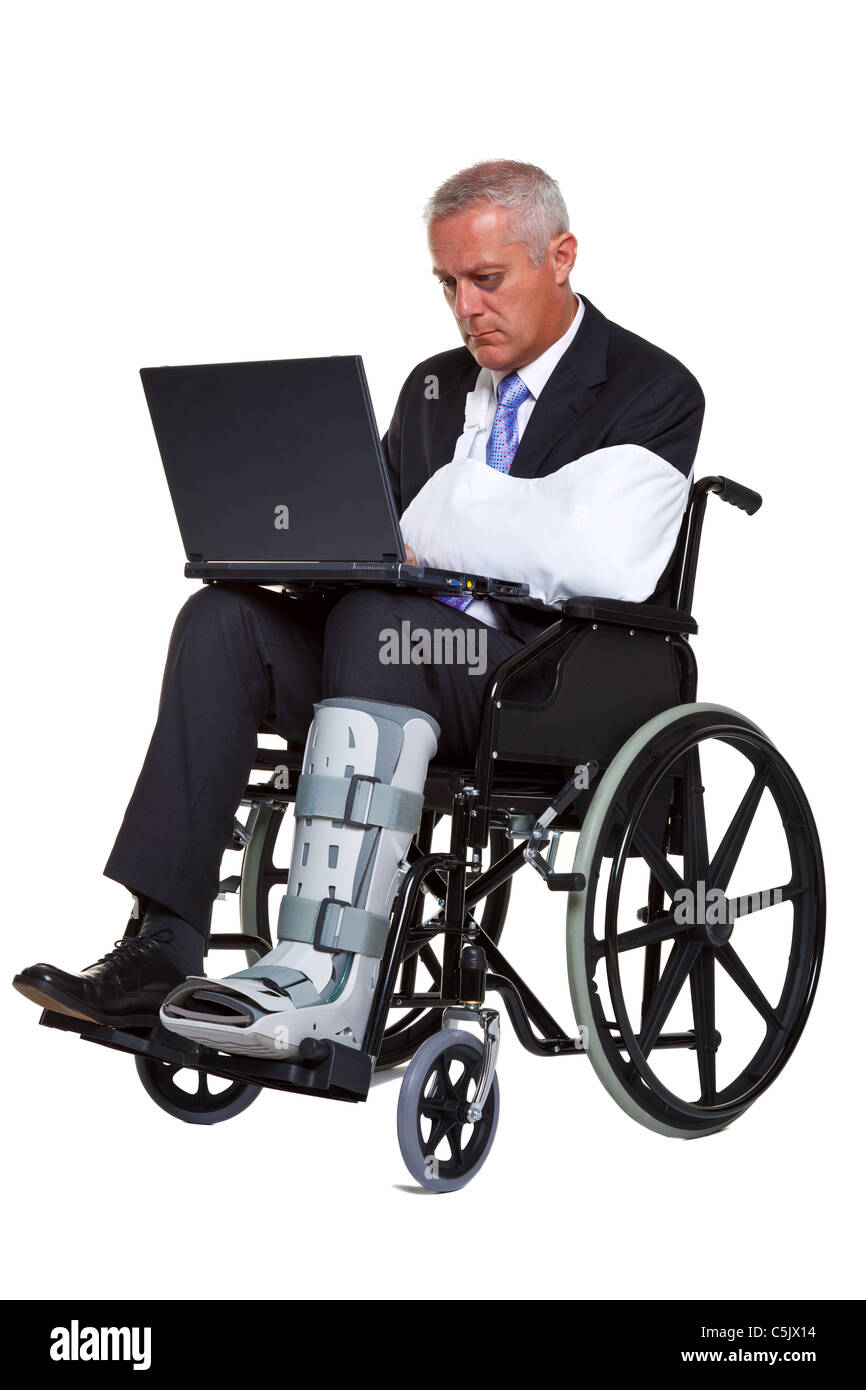 Photo d'un homme blessé dans un fauteuil roulant de travailler sur un ordinateur portable, isolé sur un fond blanc. Banque D'Images