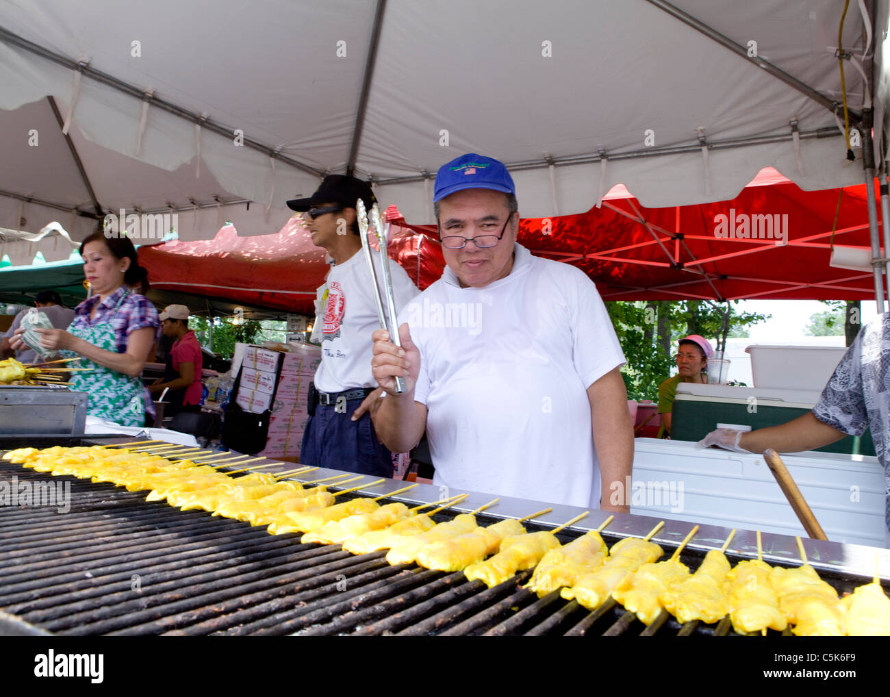 L'homme asiatique brochettes de poulet cuisson sur grill - USA Banque D'Images