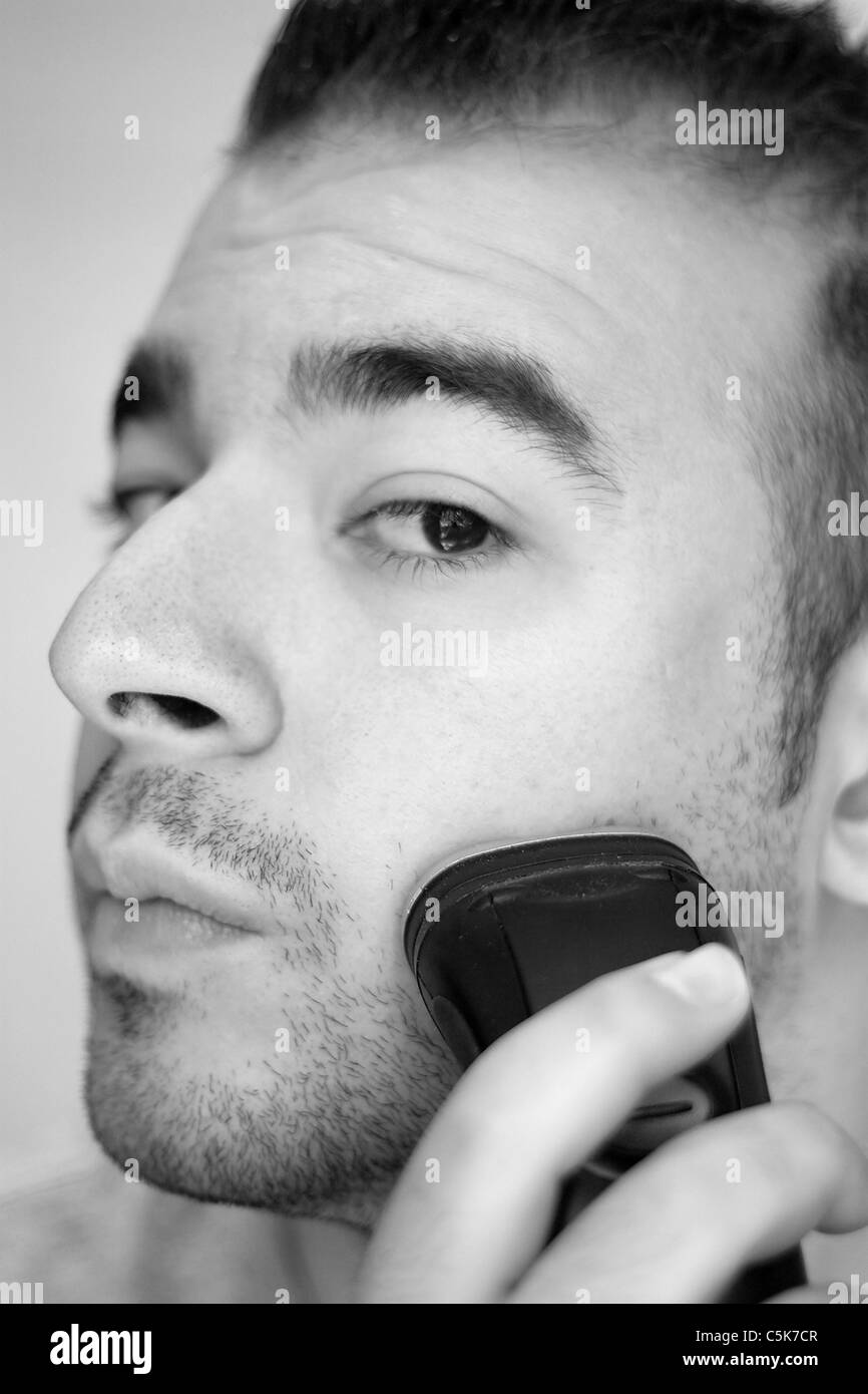 Un gros plan d'un jeune homme se raser la barbe avec un rasoir électrique  en noir et blanc Photo Stock - Alamy