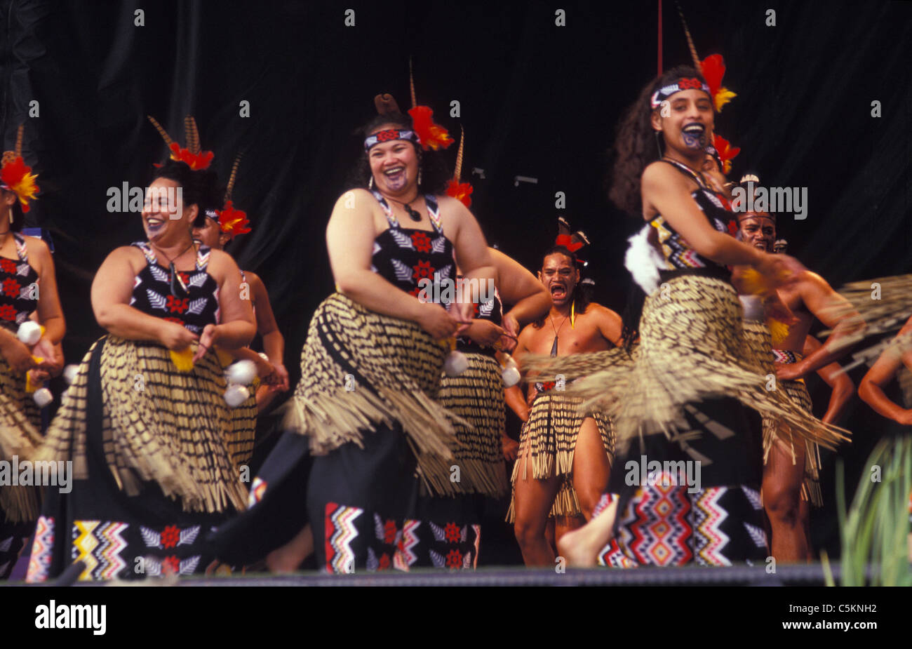 Un concert Maori chantant et dansant sur scène, les femmes à l'avant avec les pois, les hommes derrière Banque D'Images