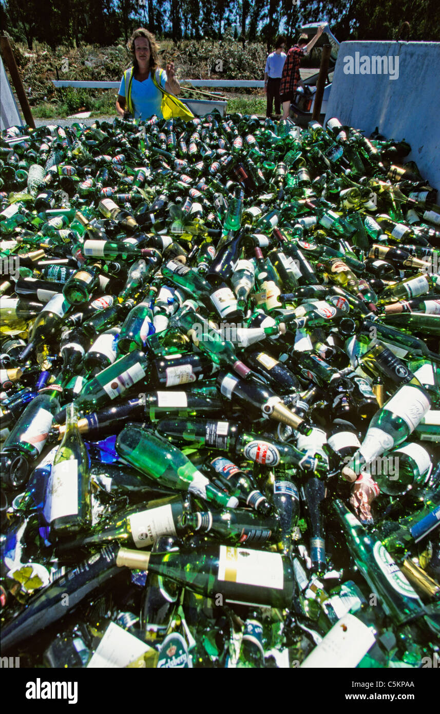 La bière vide et des bouteilles de vin à un point de collecte de recyclage avec une femme jetant une plus sur la pile, Nouvelle-Zélande Banque D'Images