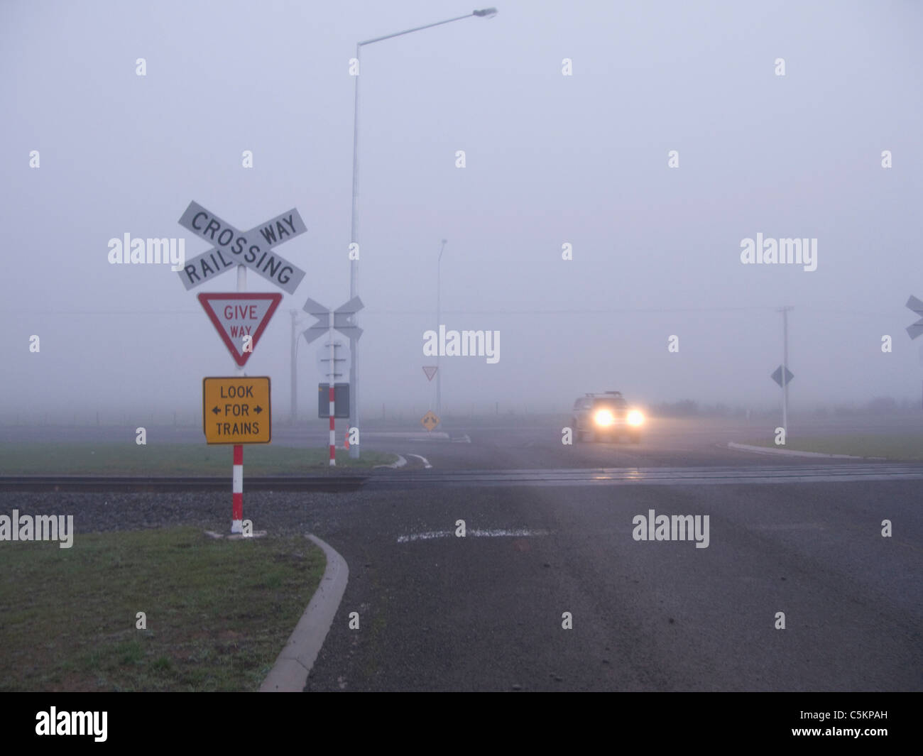 Passage à niveau dans le brouillard, avec des signes et une voiture en traversant la voie ferrée, Dunsandel, Canterbury, Nouvelle-Zélande Banque D'Images