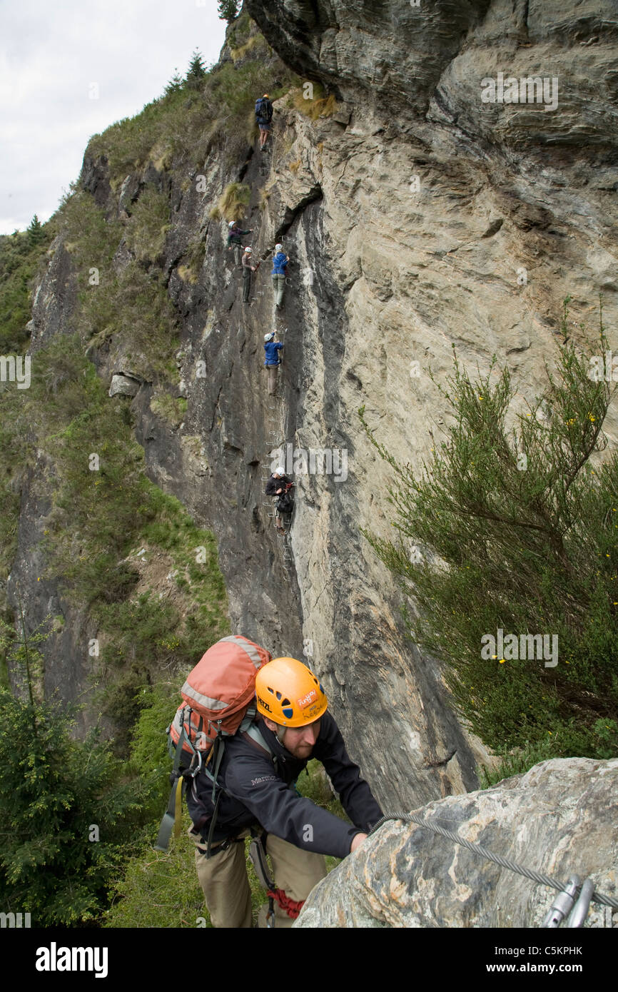 L'homme de l'escalade avec 6 personnes l'ascension d'une falaise face à l'arrière-plan, Queenstown, Nouvelle-Zélande Banque D'Images