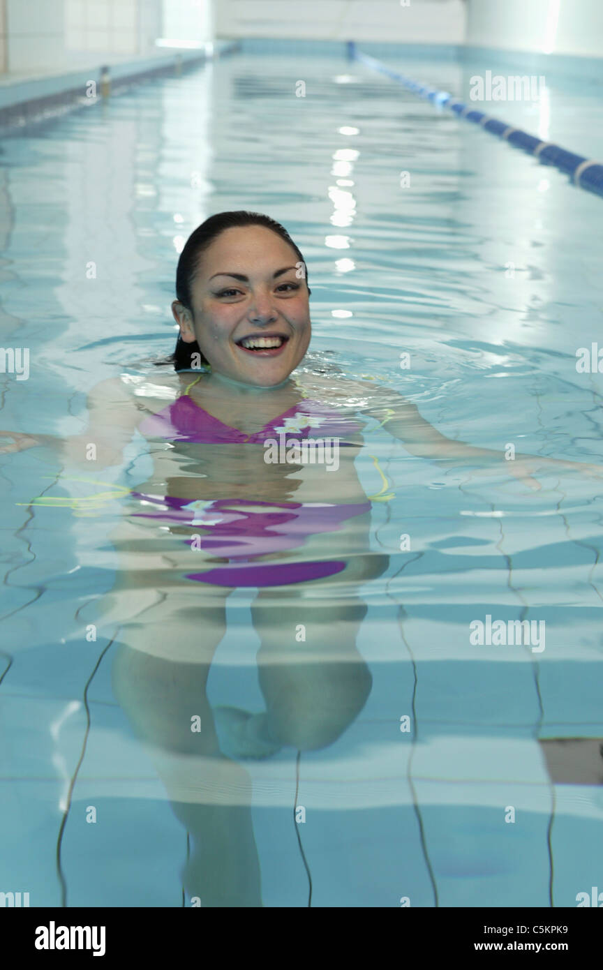 Jeune femme marchant dans l'eau piscine carrelée, smiling at camera Banque D'Images