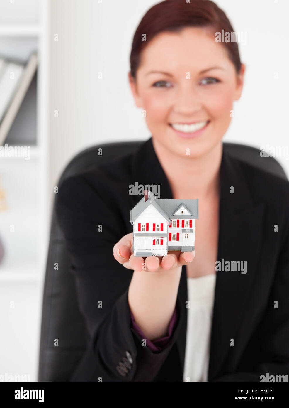 Superbe jeune femme rousse in suit holding a miniature house Banque D'Images